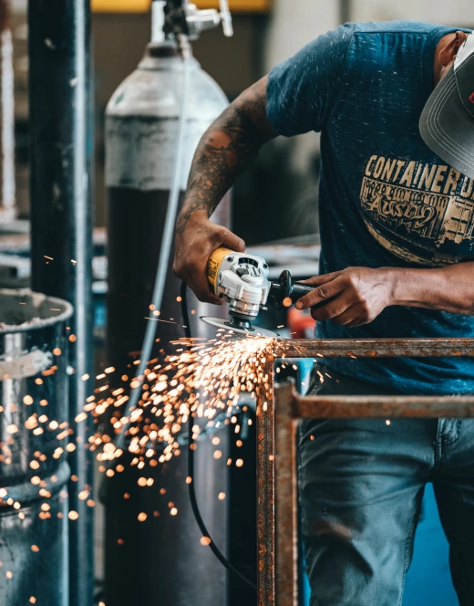 a man in a workshop grinding two steal beams